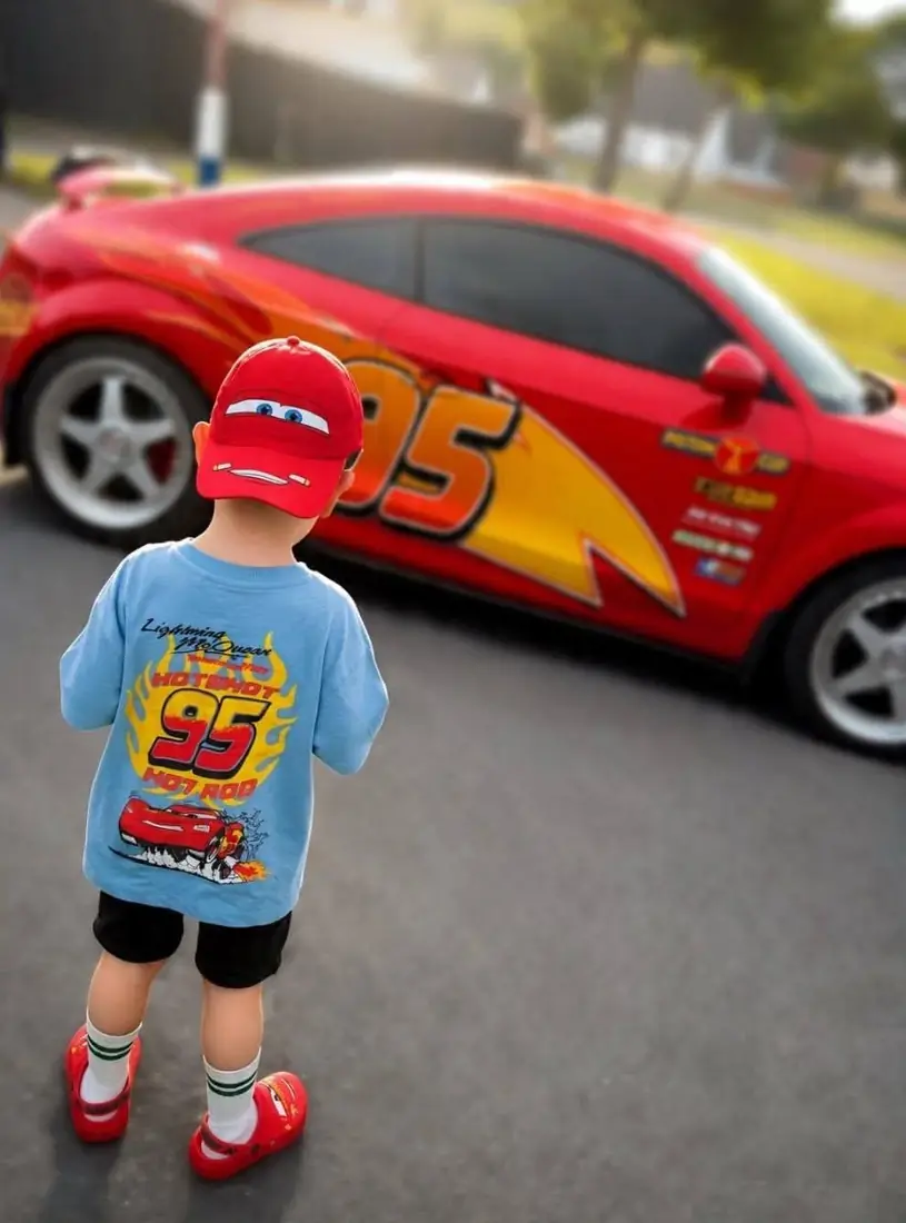 A small boy in a race car t-shirt looking at the car