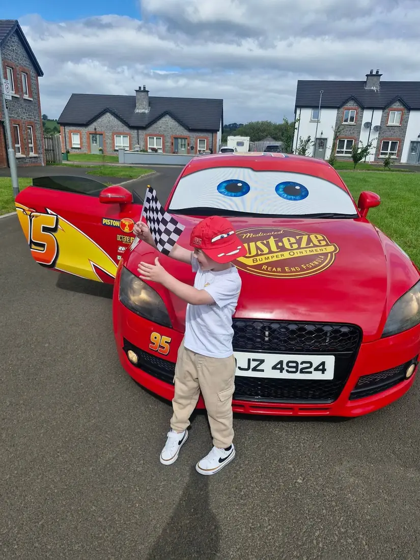 A young boy in a red cap waving a chequered flag in front of the car